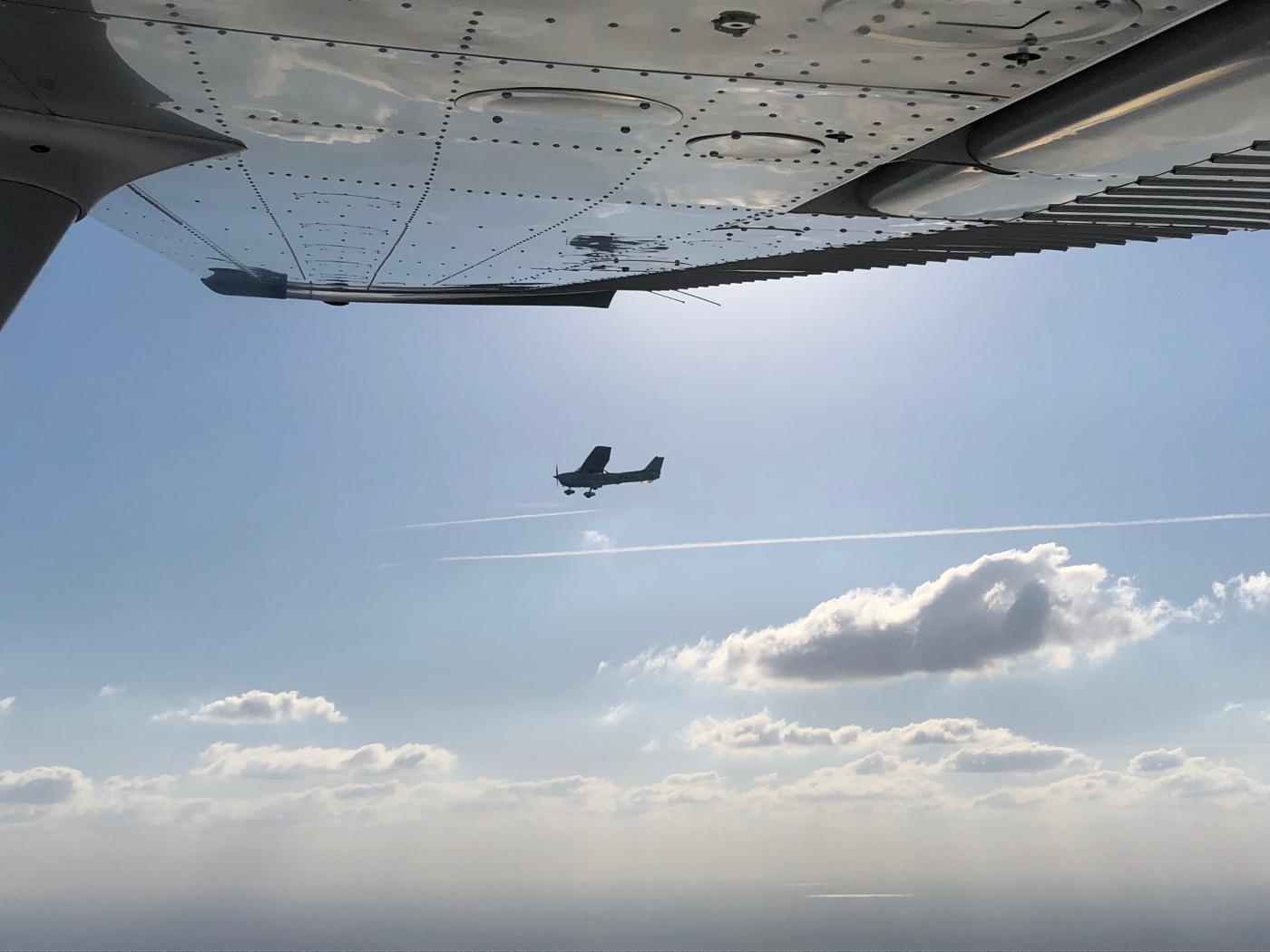 photo looking out of Cessna 172 window wing in shot, while another Cessna 172 is flying in the opposite direction