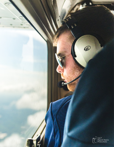 Male student flying a cessna 172 with a headset on looking out at the clouds