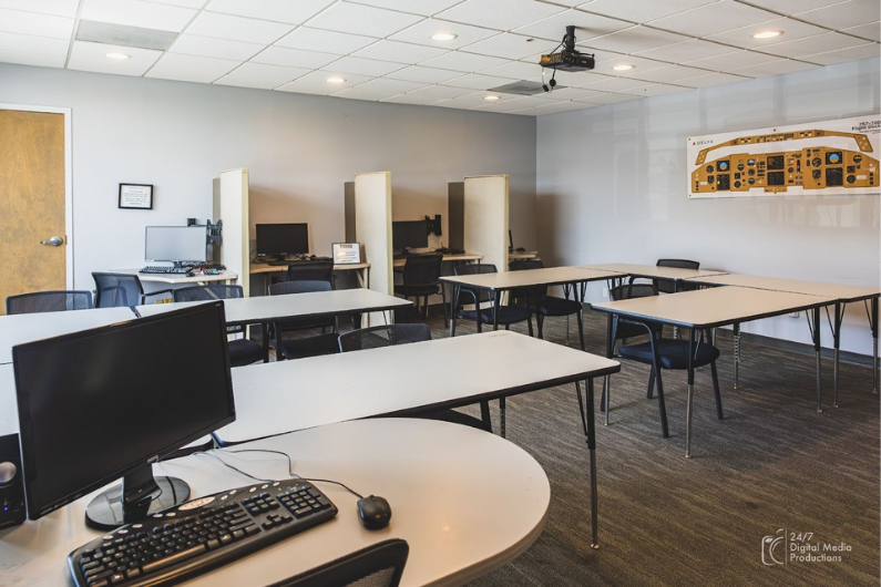 Ground school classroom a half hour outside of Atlanta, Georgia containing multiple chairs, tables, computers and a flight deck mock up on the wall