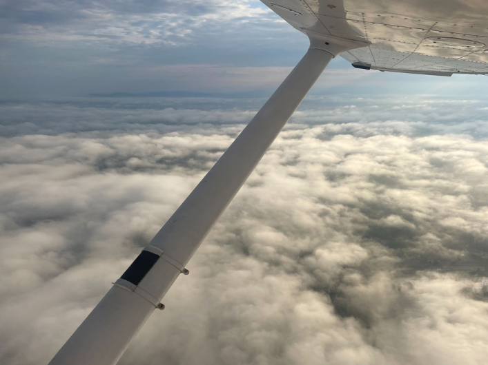 Wing of a Cessna 172 in the sky with view of clouds