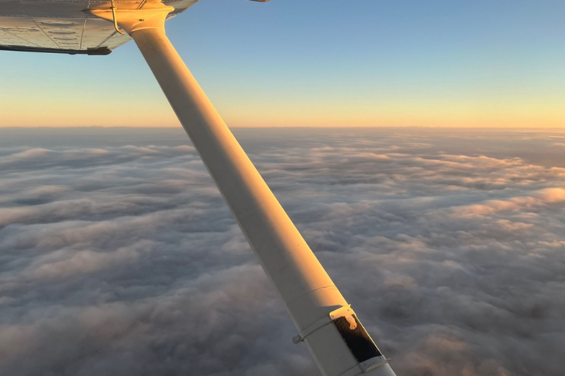 View from a Cessna 172 window of the airplane wing and strut over clouds